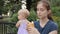 A young nanny picking pieces of a baguette and putting them into her mouth while keeping an eye on a baby girl.