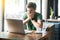 Young nervous businessman in green t-shirt sitting and working on laptop, bitting his nails and looking at screen with worry face