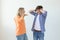 Young nervous couple wicked cute girl and upset young guy plugging ears cursing standing against white background