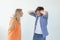 Young nervous couple wicked cute girl and upset young guy plugging ears cursing standing against white background