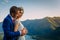 Young newly wed couple, bride and groom kissing, hugging on perfect view of mountains, river and blue sky