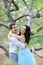 Young nice female person and brunette man hugging near blooming tree.