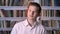 Young nice man is watching at camera, library on background