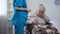 Young nurse giving medications to old lady in wheelchair, rehabilitation center