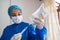 Young nurse with mask and hands in gloves preparing saline solution, holding a syringe with saline solution for patient hydration