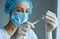 Young nurse in mask and hands in gloves preparing to injection, holding a syringe with liquid vaccine.