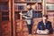 Young oldfashioned writer with typewriter in library with bearded friend