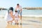 Young Parents Hold Support Cute Little Baby Toddler Girl Daughter Learning to Walk. Beach Blue Sea Sunlight. Authentic Atmosphere