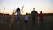 Young parents with two kids jog through grass field holding hands of each other. Mother and father with children running