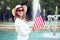 Young patriot woman in hat smilig and holding USA flag in park