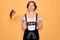 Young patriotic german woman with blue eyes wearing octoberfest dress holding germany flag happy with big smile doing ok sign,