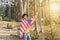 Young patriotic man in cowboy hat holding United States American flag and raising fist and arm in forest.Beautiful woodland