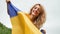 Young patriotic woman is holding blue and yellow Ukrainian flag over the sky background while celebrating visa-free