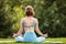 Young peaceful woman in sportswear sitting in lotus position outdoors in park and meditating