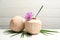 Young peeled coconuts with straw, palm leaf and flower on white wooden table