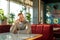 Young pensive man sitting on red velvet couch by table in classy restaurant