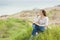 Young pensive relaxed woman in light casual clothes sitting on grass studying reading book on green field background