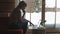 Young pensive woman sitting on the couch while typing and reading emails on the laptop with winter background on the window.