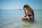 Young pensive woman in swimwear sits in the water on the coast of the ocean