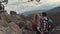 Young people climbing the mountains and holding their hands, at the top of the rock a man points at something, girl