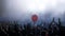 Young people with hands in the air during rock concert silhouetted against bright lights