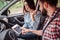 Young people are sitting in car and looking at tablet`s screen. Guy is pointing on screen. Girl is keeping her hand up.