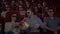 Young people sitting in movie theater watching 3D movie and eating popcorn