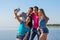 Young people - two men and two women, brunette and blonde - laugh and do selfie on the seashore