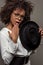 Young perplexed african american woman in white shirt wearing glasses and holding hat