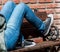 Young person with blue jeans and sneakers lying down on a wooden bench with red bricks background