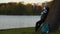 A young person in a medical mask waits for leaning on a tree on the river bank and leaves