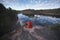 A young person on the shore of a mirror picturesque forest lake. A man photographs a picturesque landscape. Back view