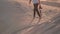 A young photographer with a camera in his hands walks barefoot on the sand of the desert in the rays of sunset