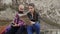 A young photographer traveling with a camera, a tourist card and a backpack sitting with a young girl on a rock and