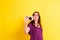 Young photography student girl holds a compact camera, isolated on yellow studio background