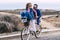 Young playful adult couple man and woman have fun together in outdoor leisure activity riding a single bike and laughing a lot -