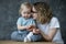 Young pleasant woman showing tiny white flowers in hand for little amazing girl baby, having fun, staring at daughter.