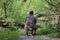 A young plump man sits on a small folding chair with his back to the camera. Sitting on the banks of the river watching the water