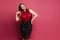 Young plus size caucasian model woman in red satin blouse and skirt posing over pink background. Gorgeous plump woman in