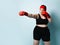 Young plus-size lady in black sporty top, shorts and red boxing gloves makes direct hit on light blue background. Martial art.