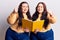 Young plus size twins holding book annoyed and frustrated shouting with anger, yelling crazy with anger and hand raised