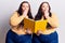 Young plus size twins holding book covering mouth with hand, shocked and afraid for mistake