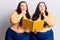 Young plus size twins holding book serious face thinking about question with hand on chin, thoughtful about confusing idea