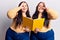 Young plus size twins holding book smiling happy doing ok sign with hand on eye looking through fingers