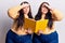 Young plus size twins holding book stressed and frustrated with hand on head, surprised and angry face