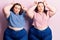 Young plus size twins wearing casual clothes doing funny gesture with finger over head as bull horns