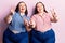 Young plus size twins wearing casual clothes smiling with tongue out showing fingers of both hands doing victory sign