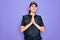 Young police woman wearing security bulletproof vest uniform over purple background praying with hands together asking for