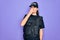 Young police woman wearing security bulletproof vest uniform over purple background smelling something stinky and disgusting,