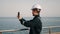 Young port worker wearing helmet and coverall making photo of amazing seaview on mobile phone